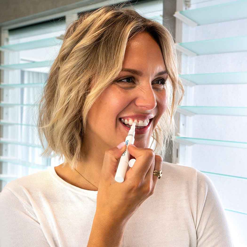 Woman smiling while applying the SmilePro teeth whitening pen