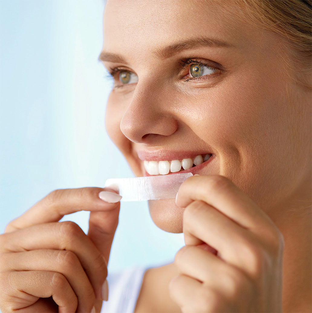 Woman smiling as she applies a SmilePro teeth whitening strip