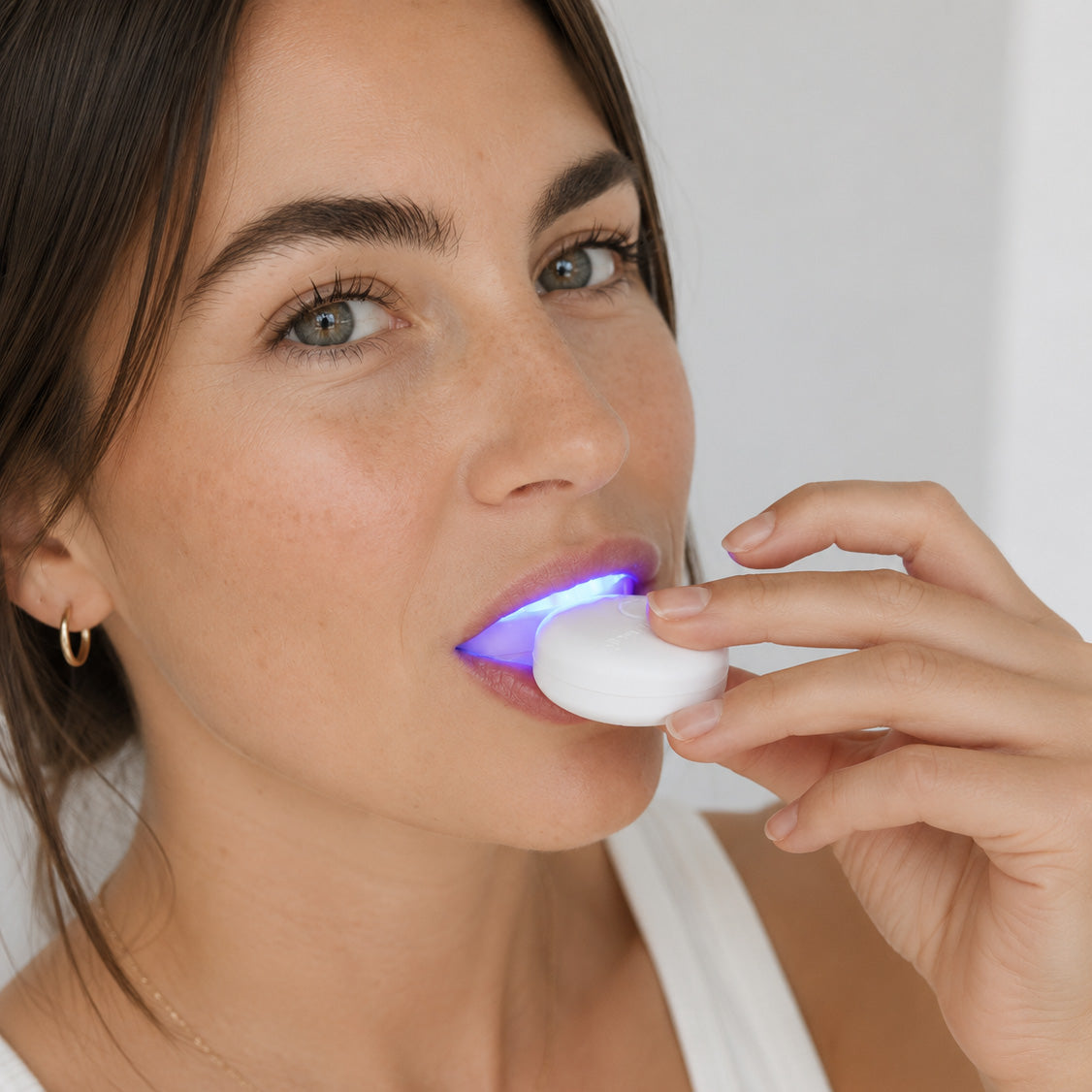 A woman using the SmilePro LED whitening light, which glows blue against her teeth, during a ten-minute treatment at home.